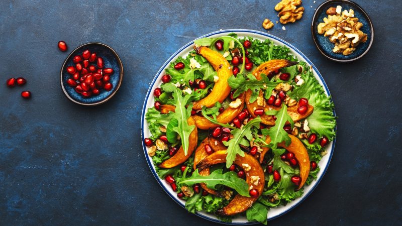 Healthy vegan eating, autumn pumpkin salad with baked honey pumpkin slices, lettuce, arugula, pomegranate seeds and walnuts. Comfort food. Top view